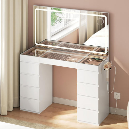 Coiffeuse vue de trois quarts : plateau en verre trempé, casiers à bijoux apparents et support sèche-cheveux latéral